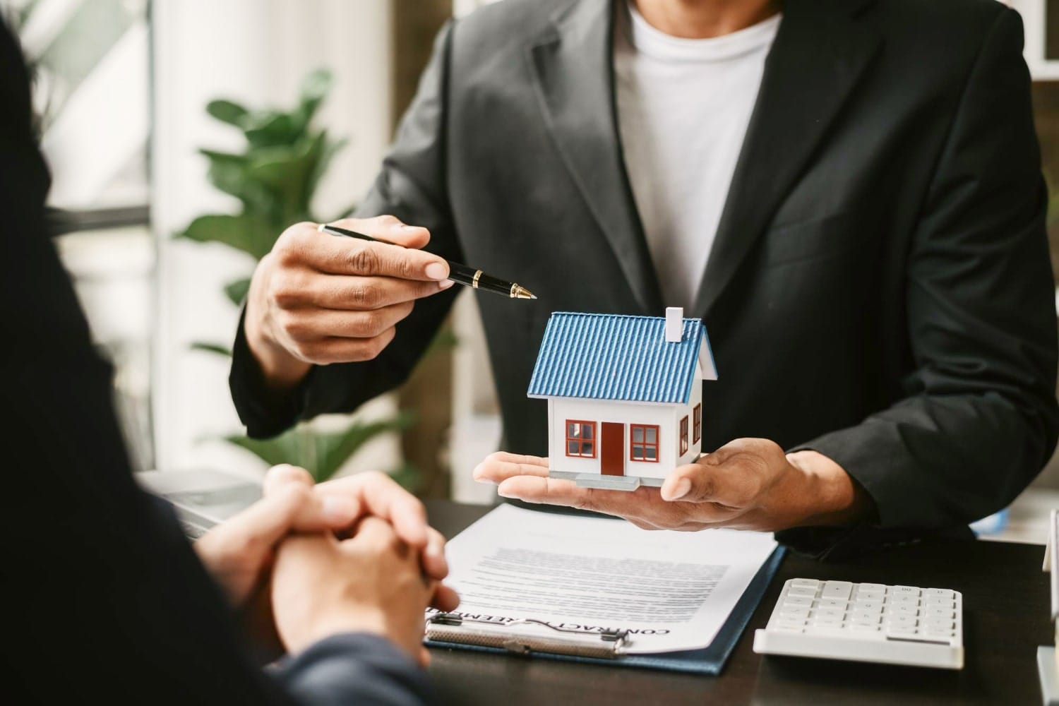 Project management: person in a suit presenting a small model house while discussing details